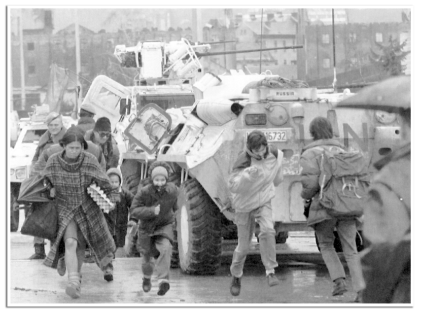 Een vrouw rent met haar kind langs een pantserwagen op de beruchte straat in Sarajevo die onder vuur ligt van scherpschutters.