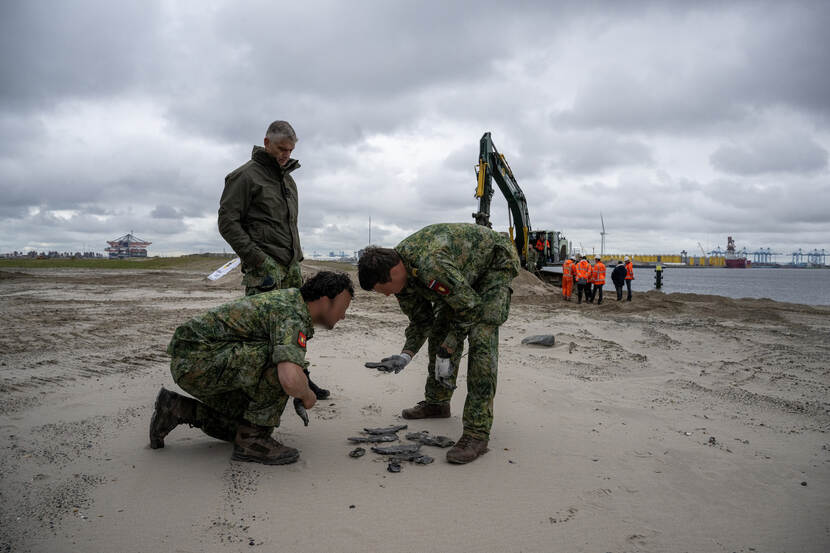 Op het zand liggen wat scherven en mannen kijken ernaar