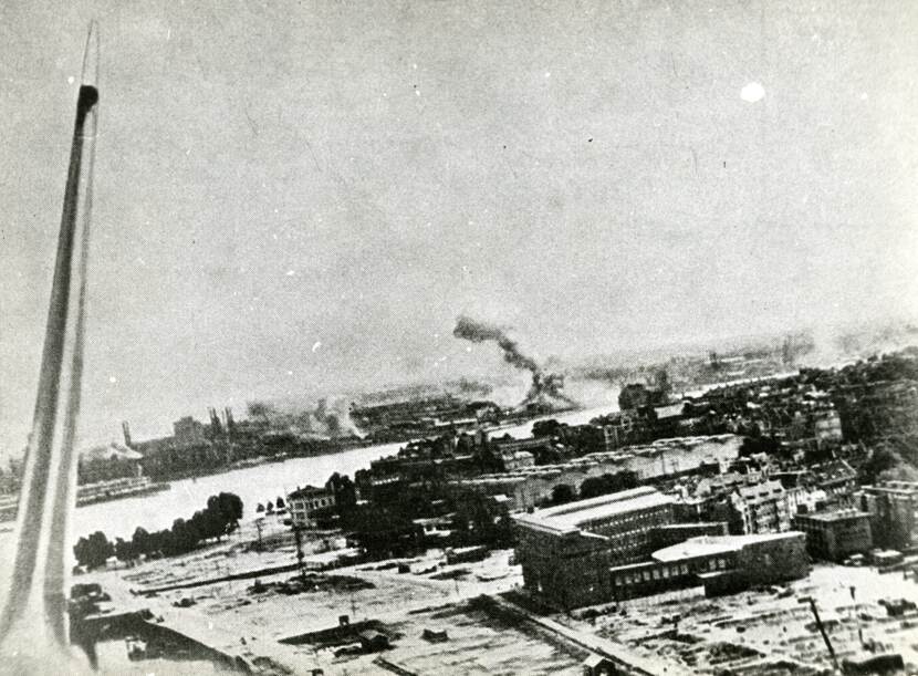 Zwart-wit foto van een deel van Rotterdam met op de achtergrond dikke rookwolken boven de Rijn- en Maashaven.