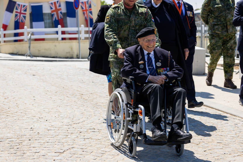 Een lachende Wolff in zijn rolstoel. Een militair duwt hem vooruit.