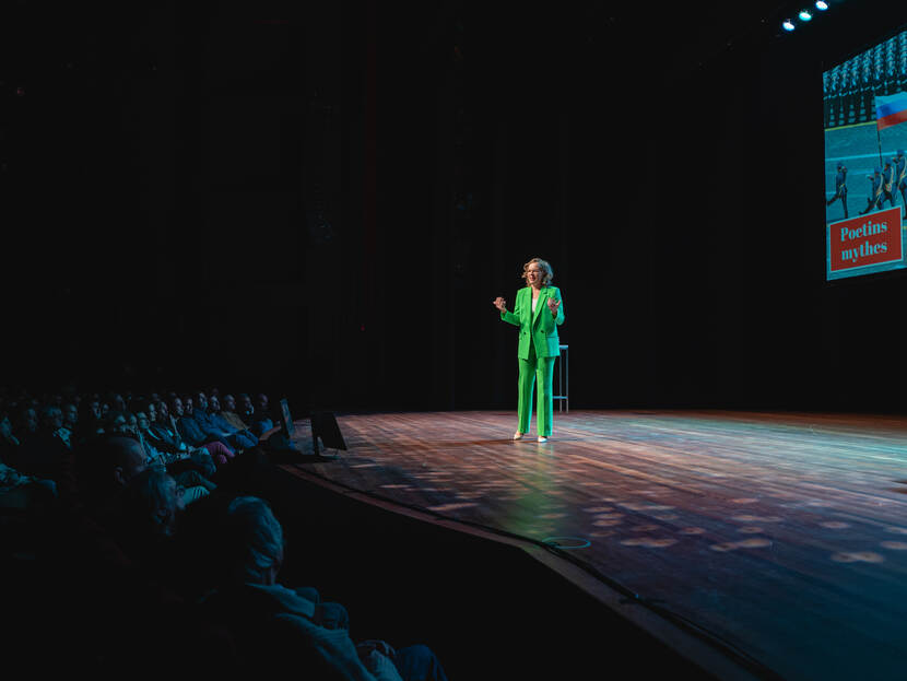Vrouw in groen pak alleen op podium voor volle zaal
