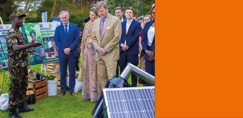 Koningspaar krijgt voorlichting van een Keniaanse militair in groen camouflagepak.