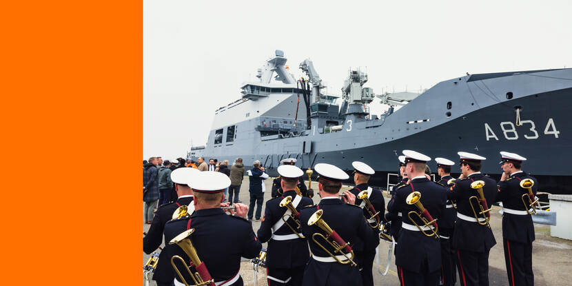 Bevoorradingsschip Den Helder, afgemeerd in de Nieuwe Haven van de Marinebasis in Den Helder. Op de kade voor het schip staat een orkest, dat het schip en de bemanning muzikaal onthaalt.