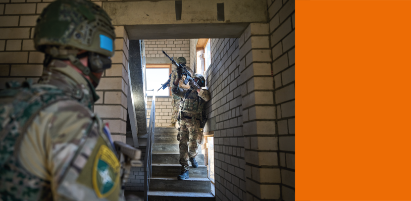 Drie militairen betreden gewapend een oefengebouw in Litouwen. Twee lopen op een trap naar boven.
