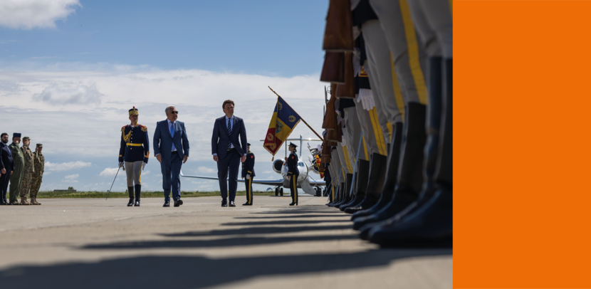 Defensieminister Ruben Brekelmans loopt over een betonnen plaat in Roemenië, geflankeerd door andere bewindspersonen en iemand in een ceremonieel tenue. Ook aan de zijkant staan militairen opgesteld in ceremonieel tenue.