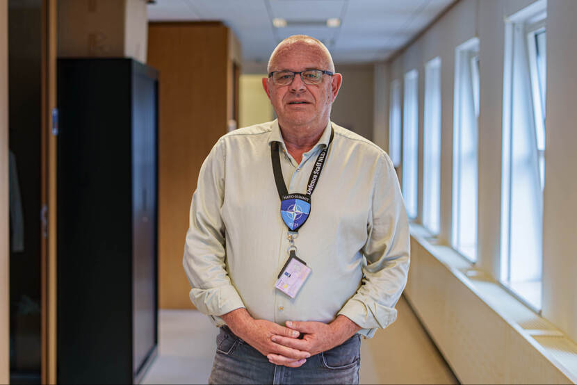 Man met badgehouder om de nek staat in gang kantoorgebouw.