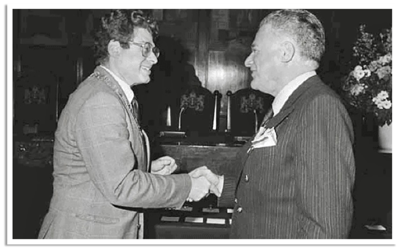 Burgermeester van Amsterdam reikt een herdenkingskruis uit aan een man.