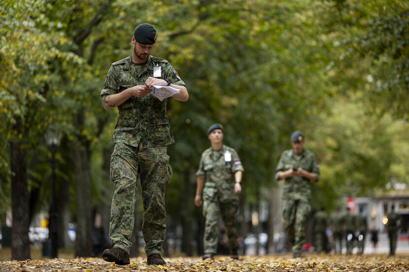 Een militair loopt met een kaart in zijn handen over een laan. Deze is bedekt met bladeren. Achter hem lopen nog twee militairen.