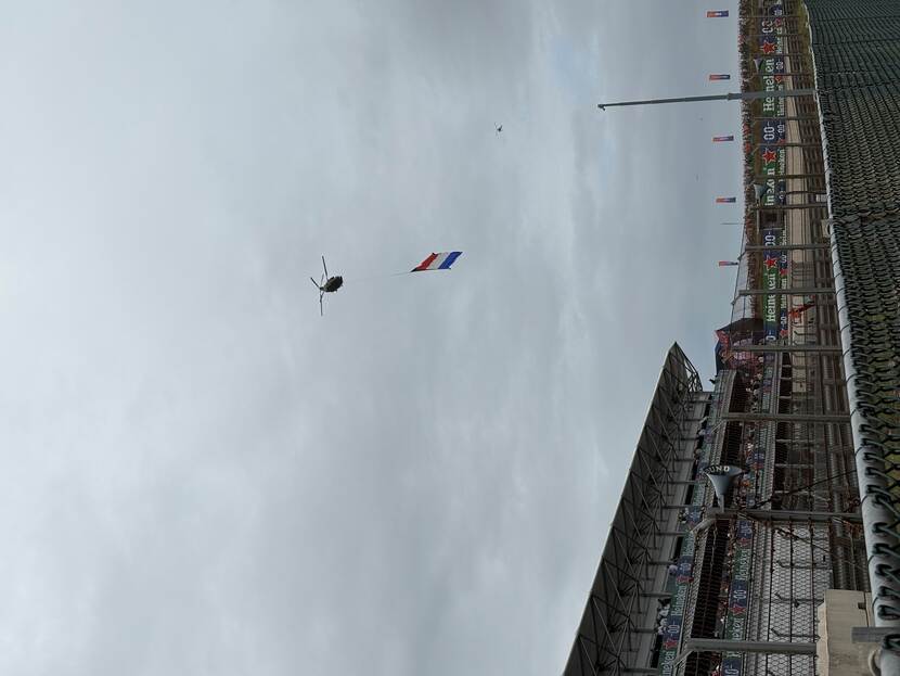 Helikopter vliegt over een circuit, eronder hangt de Nederlandse vlag