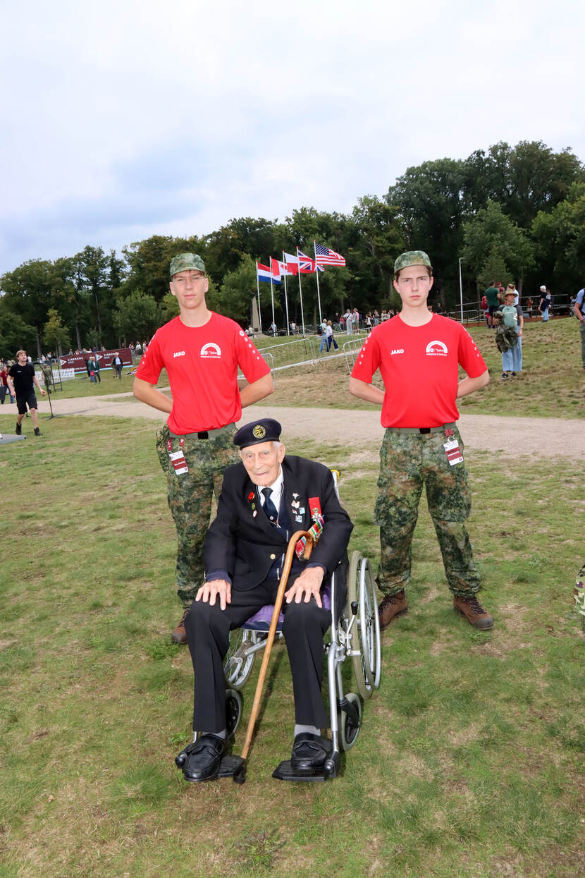 Twee studenten flankeren de in een rolstoel gezeten Britse veteraan.