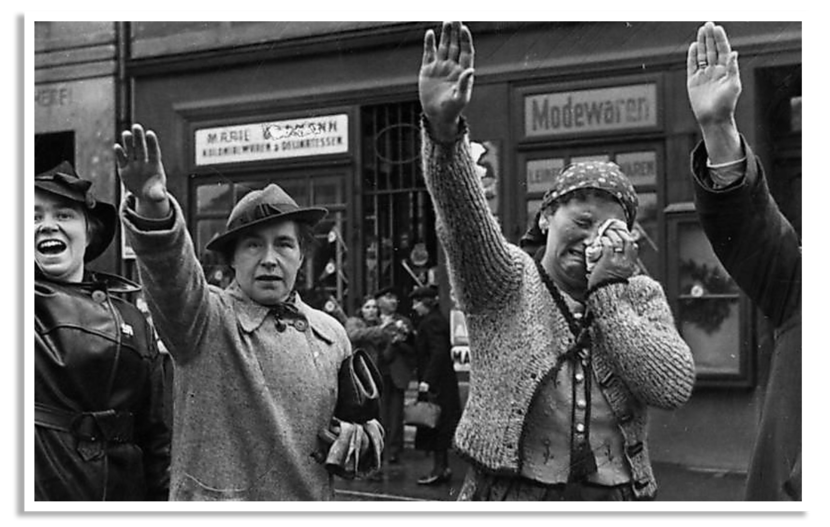 Drie vrouwen brengen de Hitlergroet als Duitse militairen Sudetenland intrekken.