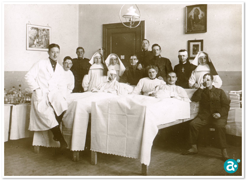 Een groep artsen, verplegers, nonnen en soldaten staat rondom een gewonde patiënt in een bed in een oude ziekenhuiskamer met medische flessen en eenvoudige meubels.