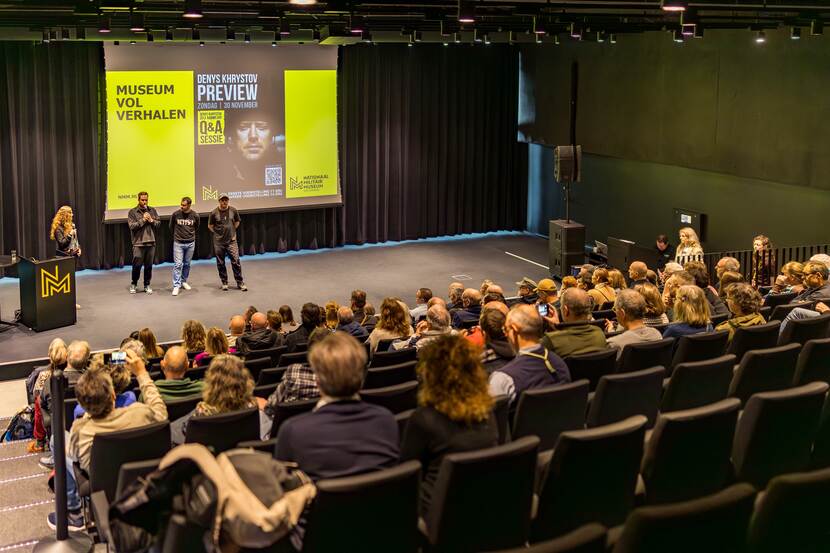 zicht op de filmzaal van het NMM met Denys en een aantal andere sprekers staande op het podium.