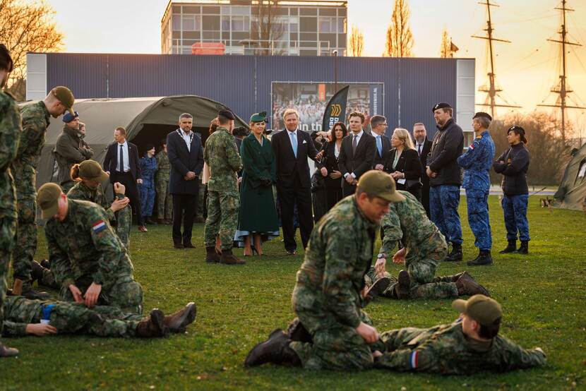 Militairen in opleiding trainen terwijl op de achtergrond de koning en zijn gasten toekijken.
