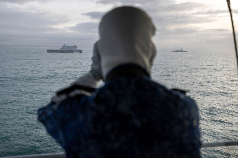 Een matroos tuurt met een verrekijker naar buiten.