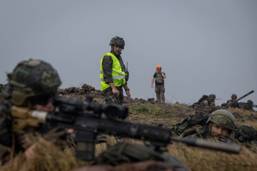 Een gevechtschietinstructeur kijkt kritisch naar een geweerschutter.