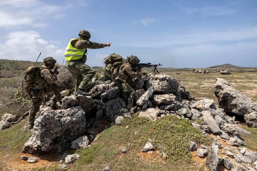 Een gevechtschietinstructeur geeft aanwijzingen aan een mitrailleurschutter. Naast hen zijn uitkijk.