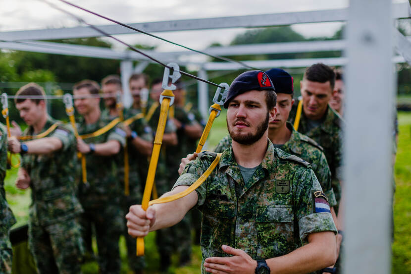 Een rij mariniers zit met gele koorden vastgeklikt aan een kabel boven hun hoofd.