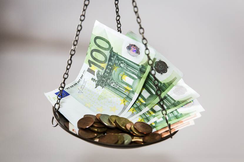 Een weegschaal met bankbiljetten en muntjes erop.