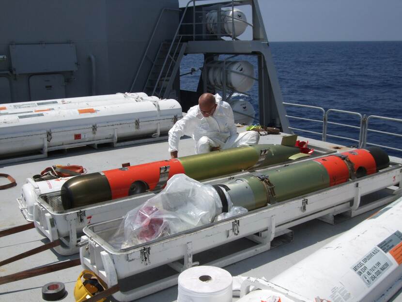 Een technicus verpakt een torpedo op het achterdek van een schip.