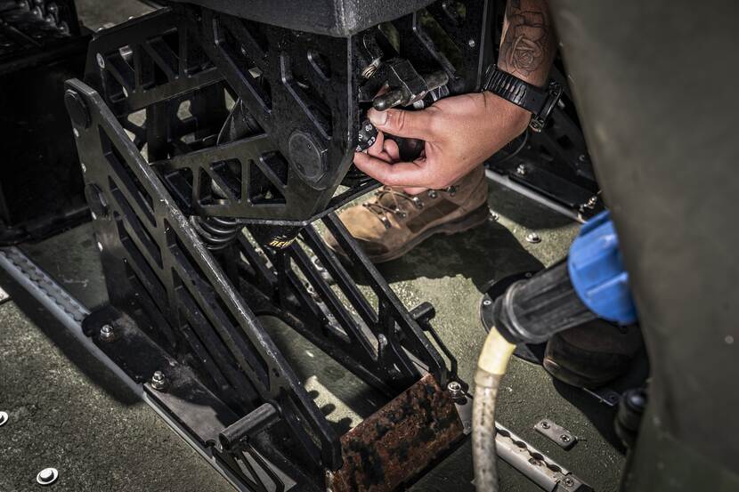 Een hand draait aan de knop voor het instellen van de stoelvering.