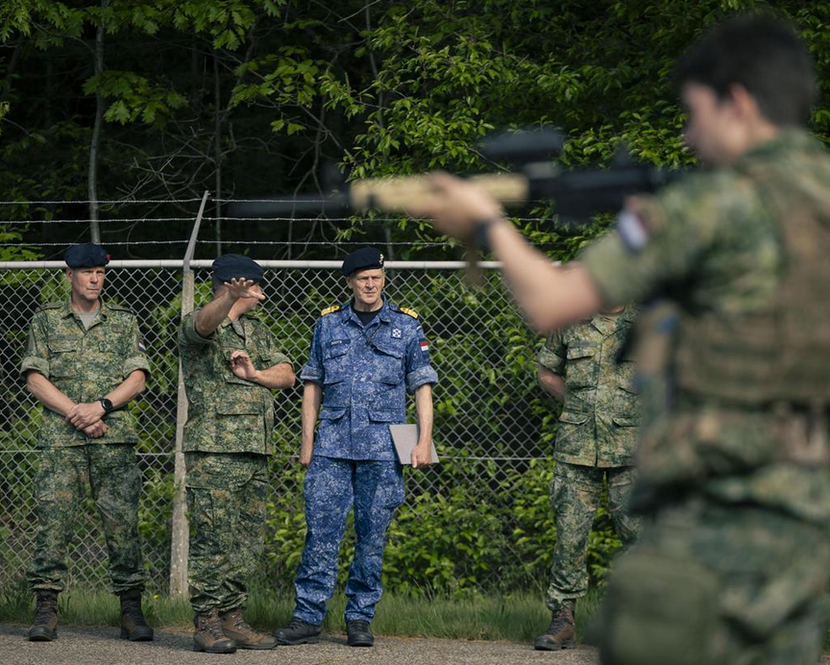 Op de achtergrond een rijtje militairen met de IGK in het midden. Op de voorgrond een schutter.