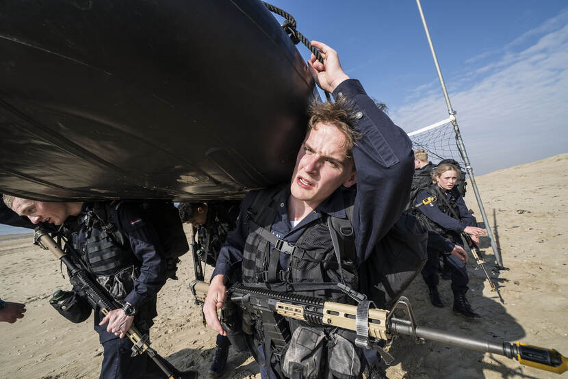 Matrozen in opleiding dragen een rubberboot door de duinen.