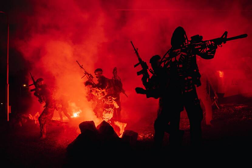 Mariniers rennen gewapend voorwaarts door rode rook en rood licht. Ook zijn de uitsneden van staal te zien.