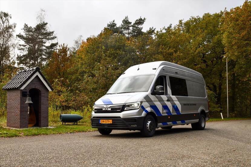Beeld van een metallic grijze bus met witte en blauwe strepen.