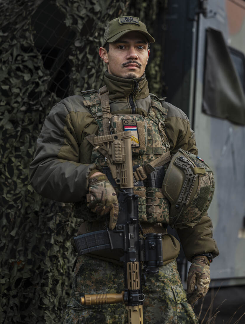 Een gewapende militair staat voor zijn gecamoufleerde voertuig.