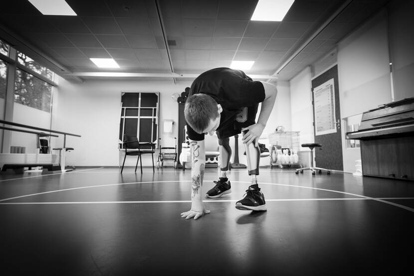 Illia steunt met zijn rechterhand op vloer terwijl hij omhoogkomt om weer rechtop te staan.