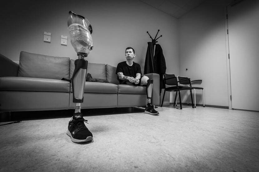 Eén van Illia’s protheses staat op de voorgrond. Zelf zit hij op de achtergrond op een bank.