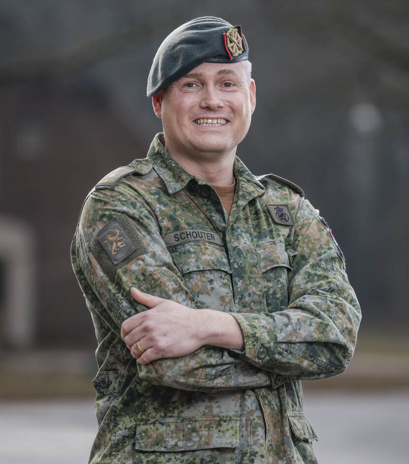 Een majoor in militaire outfit poseert breed lachend en met armen over elkaar