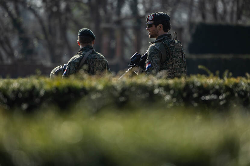 2 militairen houden de wacht achter een heg.
