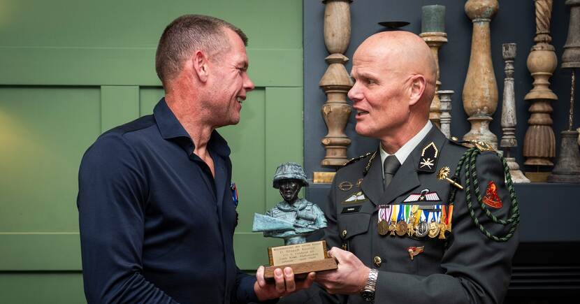 Militair overhandigt bronzen beeld aan veteraan in burger.