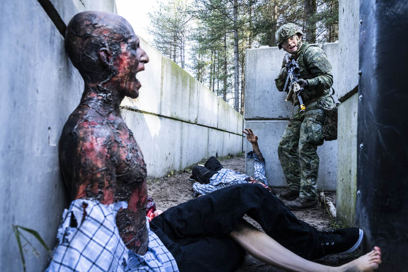 Een soldaat kijkt om zich heen in een loopgraaf. Een bebloede dummy op de voorgrond