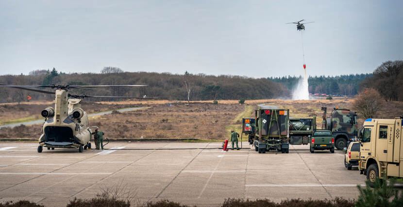 Op de voorgrond wordt een Chinook bijgetankt vanuit een tankwagen, op de achtergrond leegt een Chinook zijn bluszak.