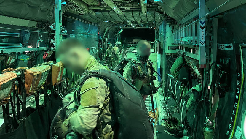 Onherkenbaar gemaakt defensiepersoneel staat in het laadruim van een C-130.