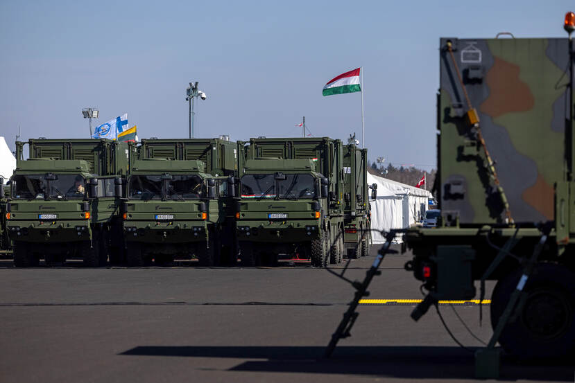 Een drietal legertrucks naast elkaar opgesteld, daarachter wappert een Hongaarse vlag.
