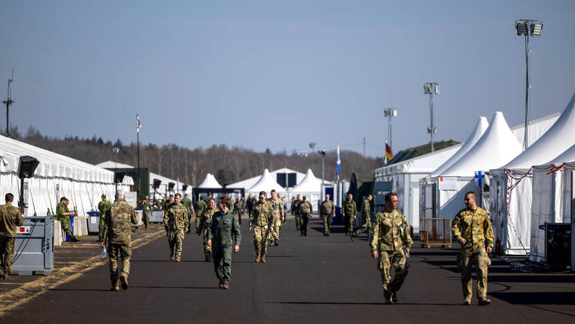 Militairen die langs witte tenten lopen.
