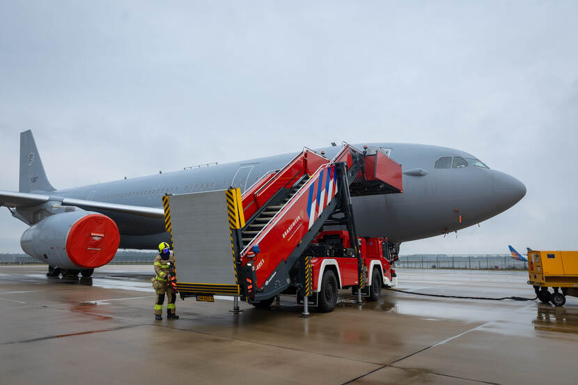 Het rode Rescue Stair Vehicle geplaatst tegen een grijs militair vliegtuig.