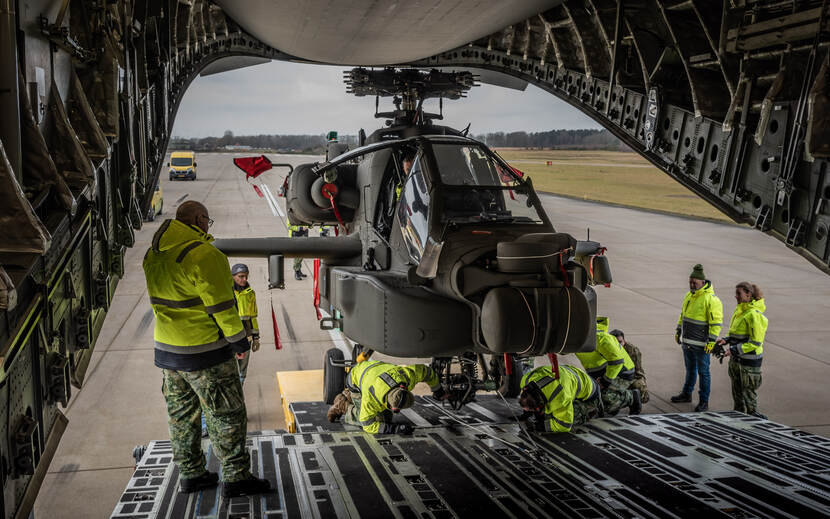 Foto vanuit de buik van de C-17 waarbij een van de twee Apaches naar buiten wordt gerold door mensen in felgele jassen.