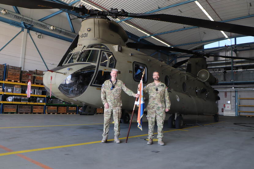Spitshoven en Peterse poseren met een vlag tussen beiden in een hangaar voor een Chinook.