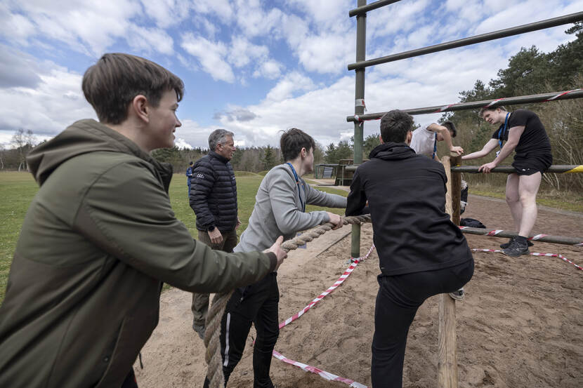 Deelnemers klimmen over houten balken en een stalen rek.