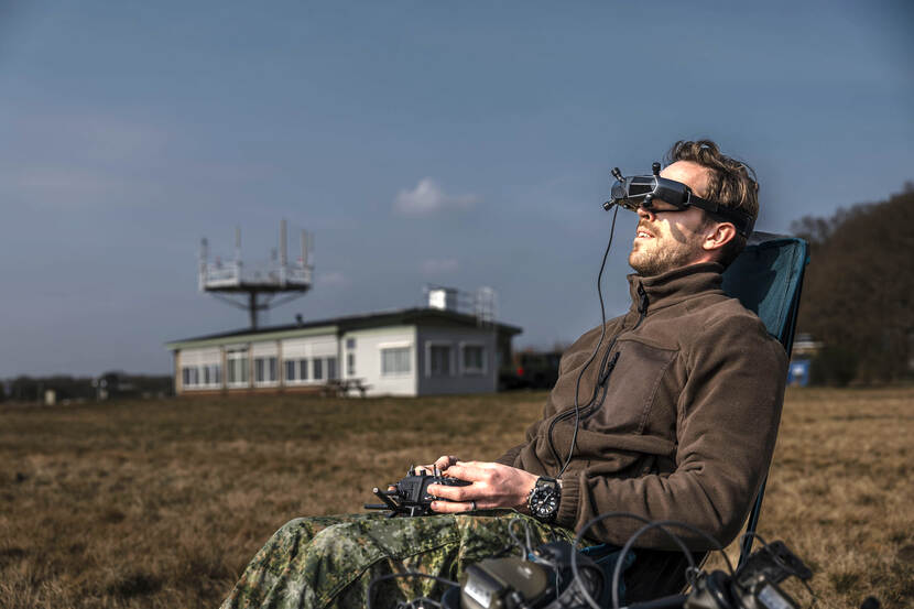 Een militair met een VR-bril op in een stoel op een grasveld.