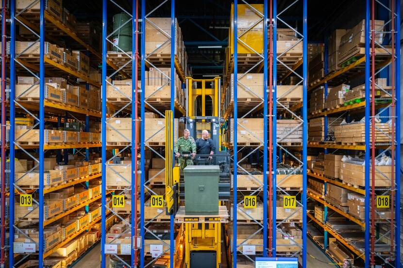 Twee mensen op hoogte op een heftruck in een magazijn vol hoge stellingen.