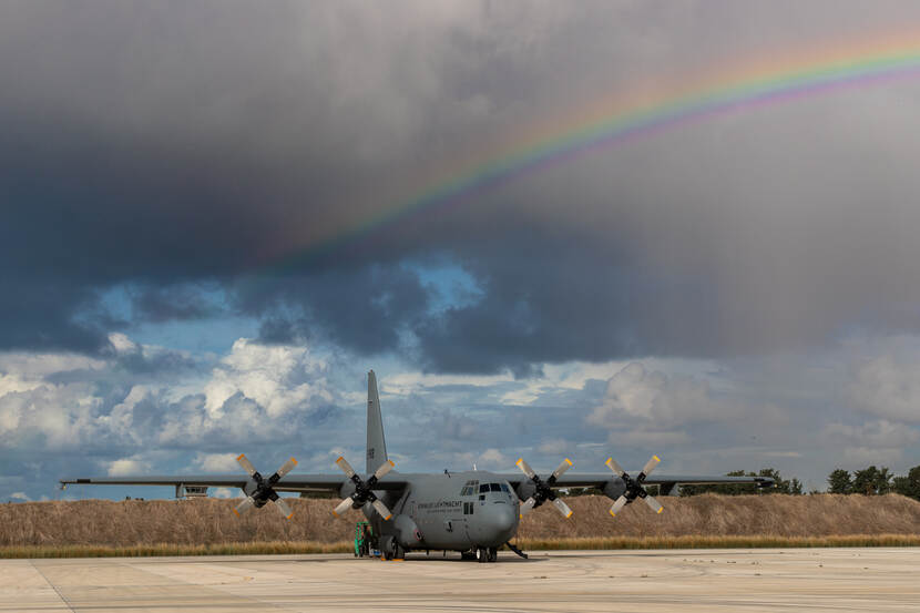 C-130 op een platform onder donkere wolken en een regenboog.
