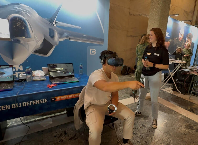Jongeman in burgerkleding met een VR-bril op bij een luchtmachtstand van ‘Werken bij Defensie’.