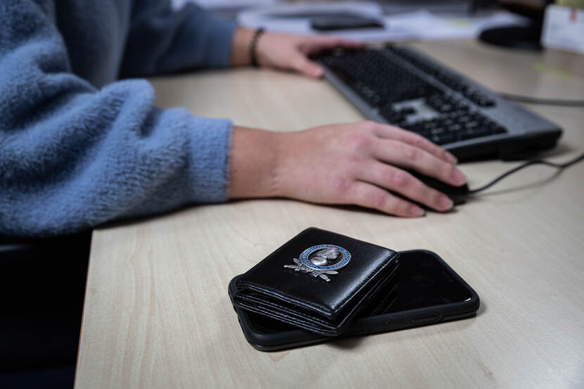 Marechausseebadge op de voorgrond. Handen op een toetsenbord op de achtergrond.