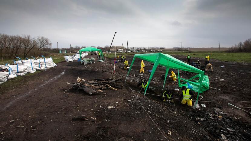 Mannen in gele pakken zoeken systematisch op de crashsite. Er staan tenten en de grond is onderverdeeld in rasters.